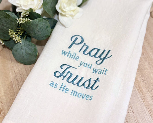 White towel with inspirational embroidered quote on a wooden surface with flowers