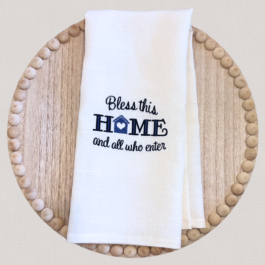 White linen towel with 'Bless this home and all who enter' text on a wooden plate