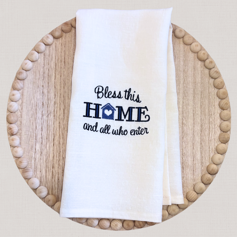 White linen towel with 'Bless this home and all who enter' text on a wooden plate
