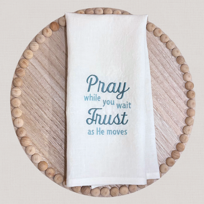White linen towel with blue embroidered text on a wooden tray