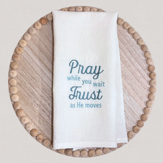 White linen towel with blue embroidered text on a wooden tray