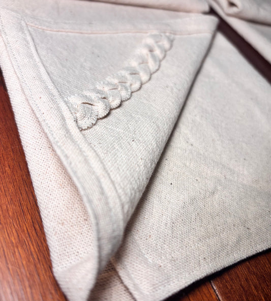Close-up of a light gray fabric with embroidered trim on a wooden surface