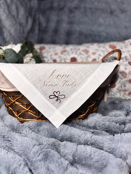 linen handkerchief with 'Love Never Fails' text on a textured surface