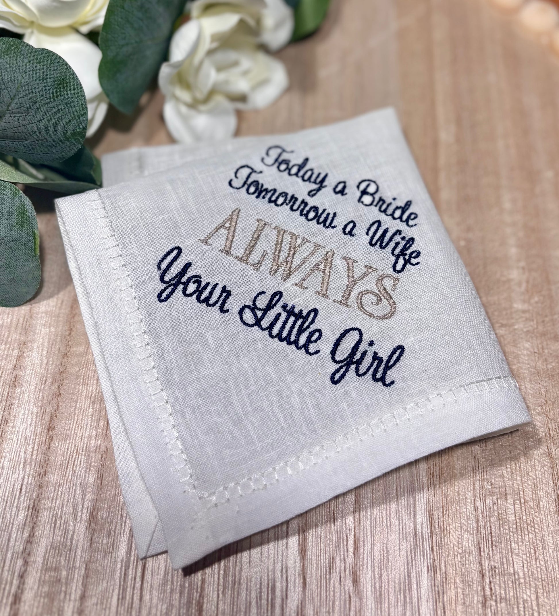 Embroidered handkerchief with text on a wooden surface with flowers in the background