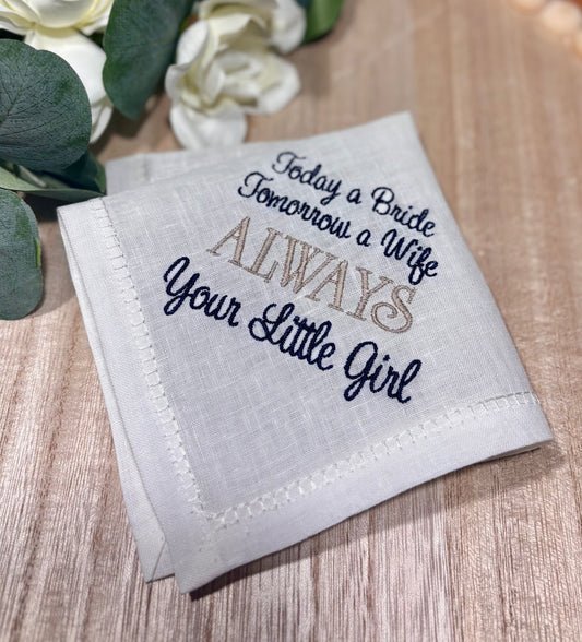 Embroidered handkerchief with text on a wooden surface with flowers in the background